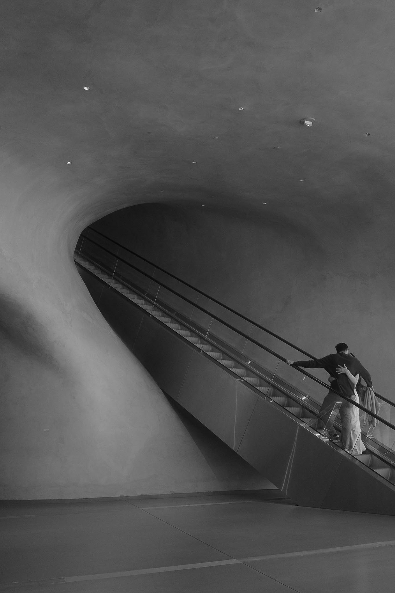 Figure ascending a curved escalator in monochrome architecture